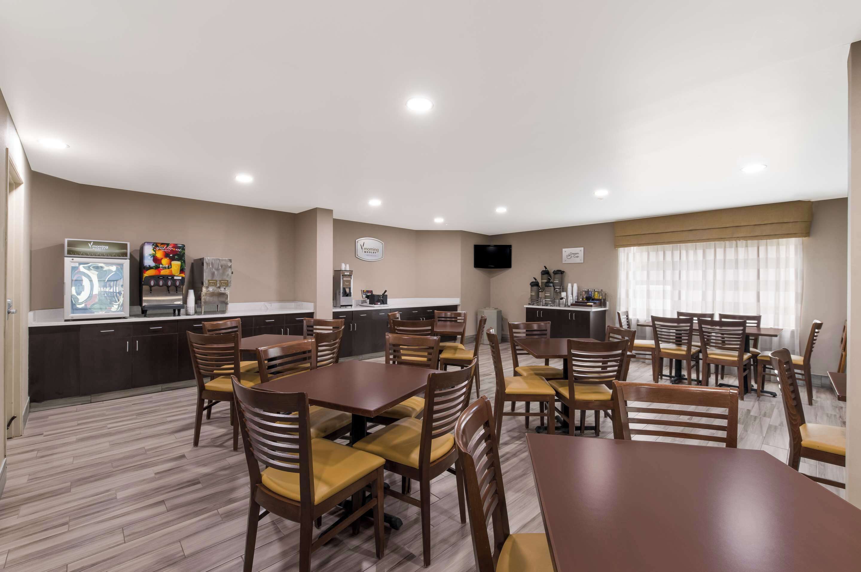 A dining area with wooden tables and chairs, a kitchen area with appliances, and a television on the wall.