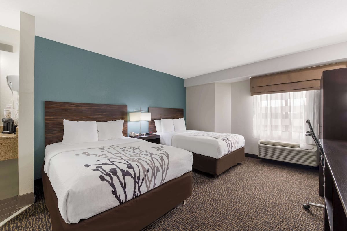 A hotel room with two beds, a desk with a lamp, a TV, and a window with curtains.