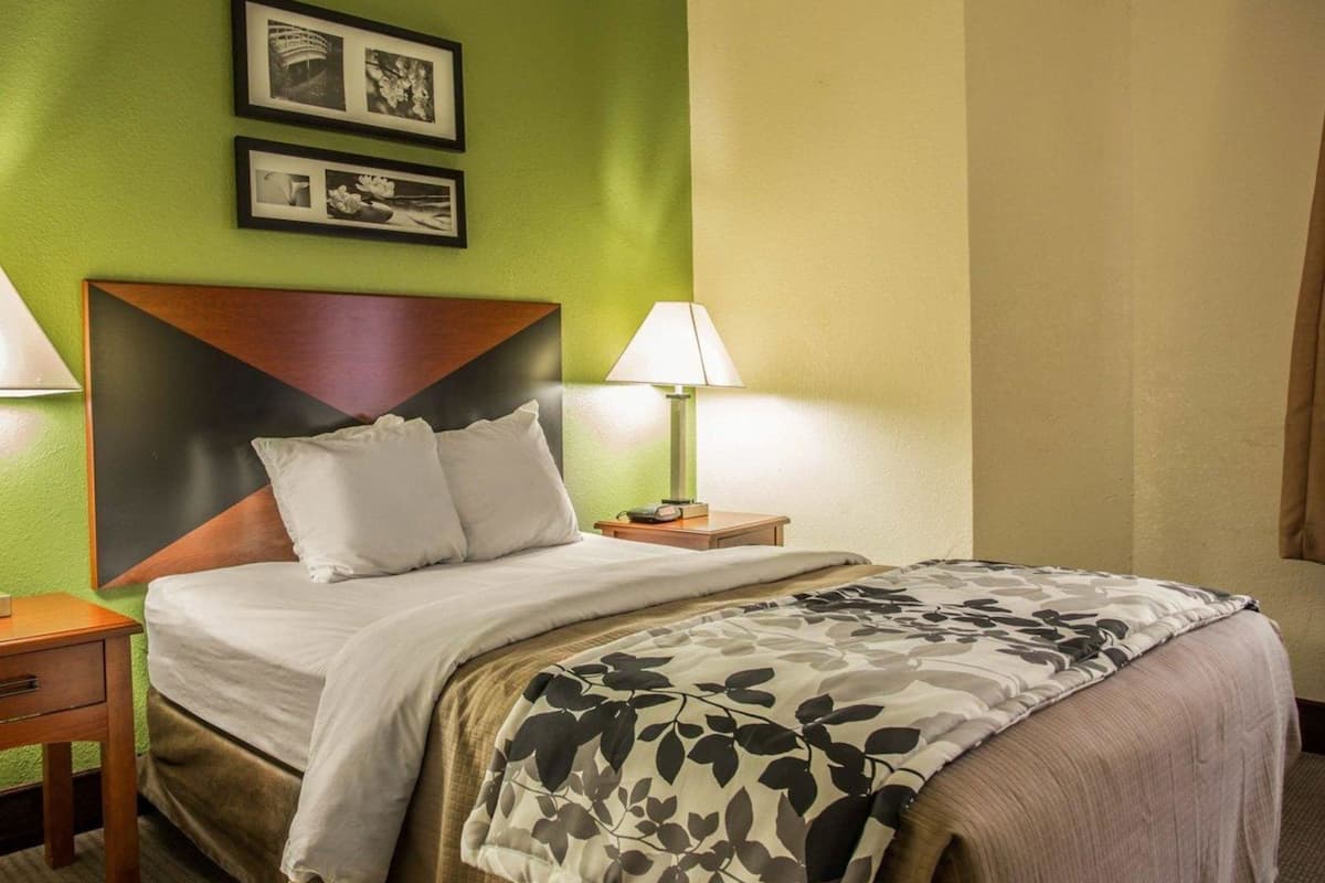 A hotel room with a bed, two bedside lamps, a headboard, and two framed pictures on the wall.