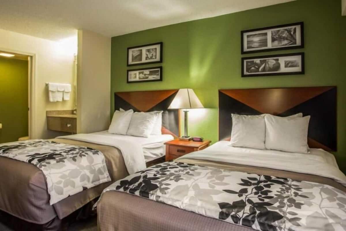 A hotel room with two beds, a nightstand, a lamp, and framed pictures on the wall.