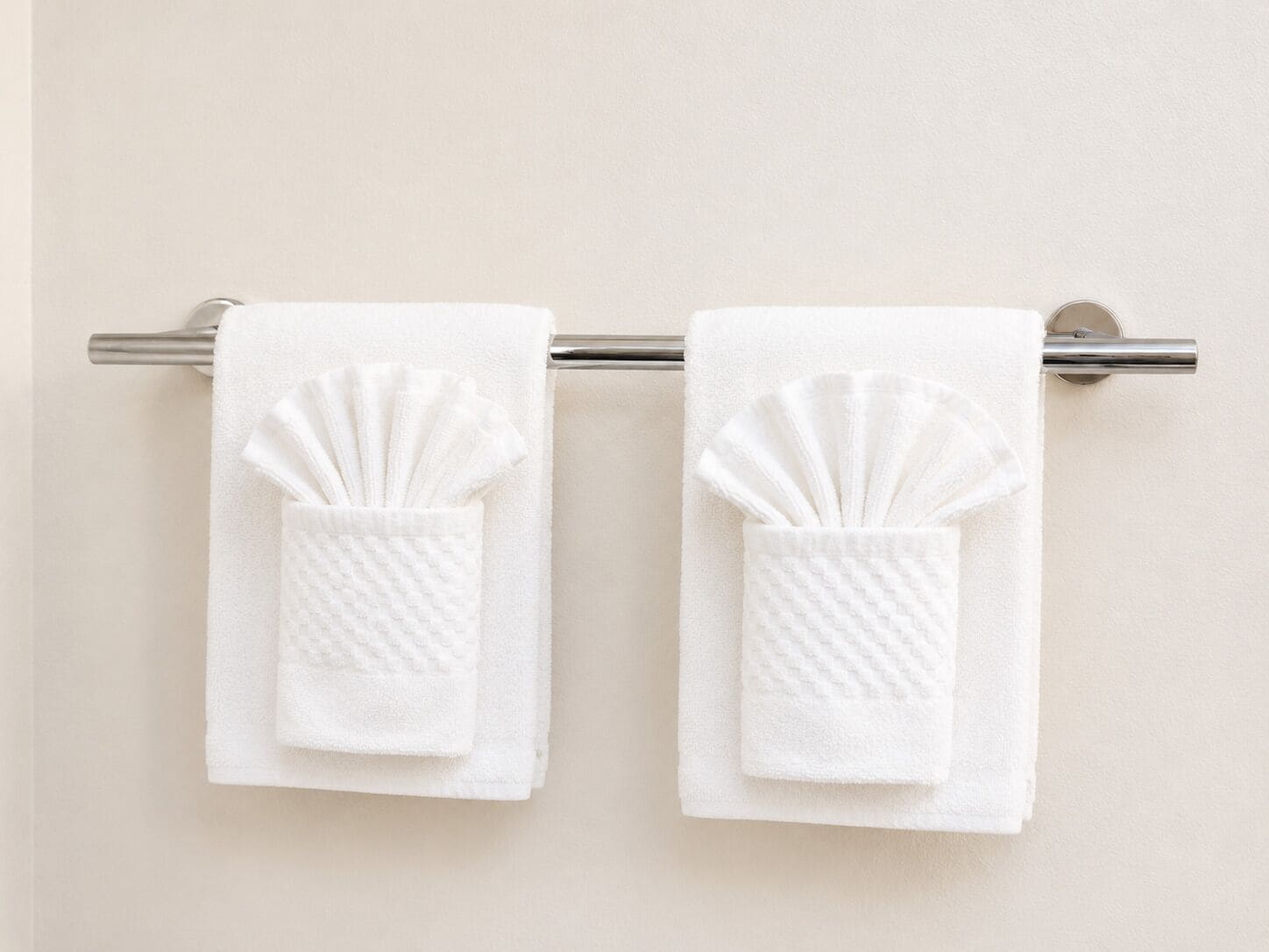 Two white towels with a textured pattern hanging on a metal towel rack against a plain wall.