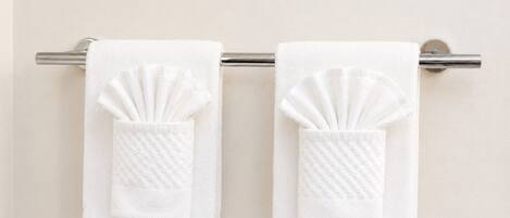Two white towels with a textured pattern hanging on a metal towel rack against a plain wall.