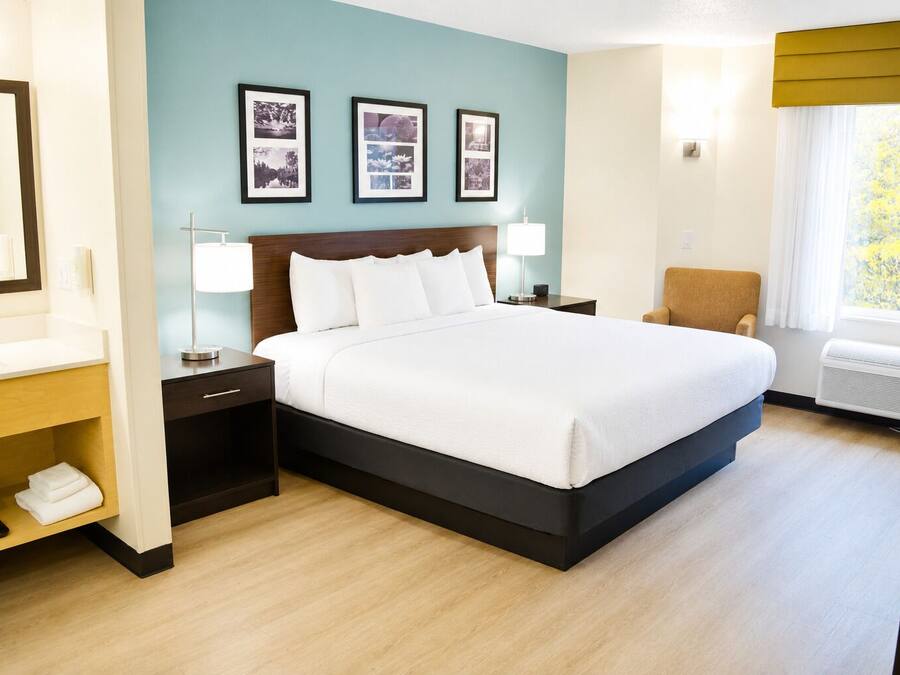 A hotel room with a bed, bedside tables, a chair, a mirror, and framed pictures on the wall.