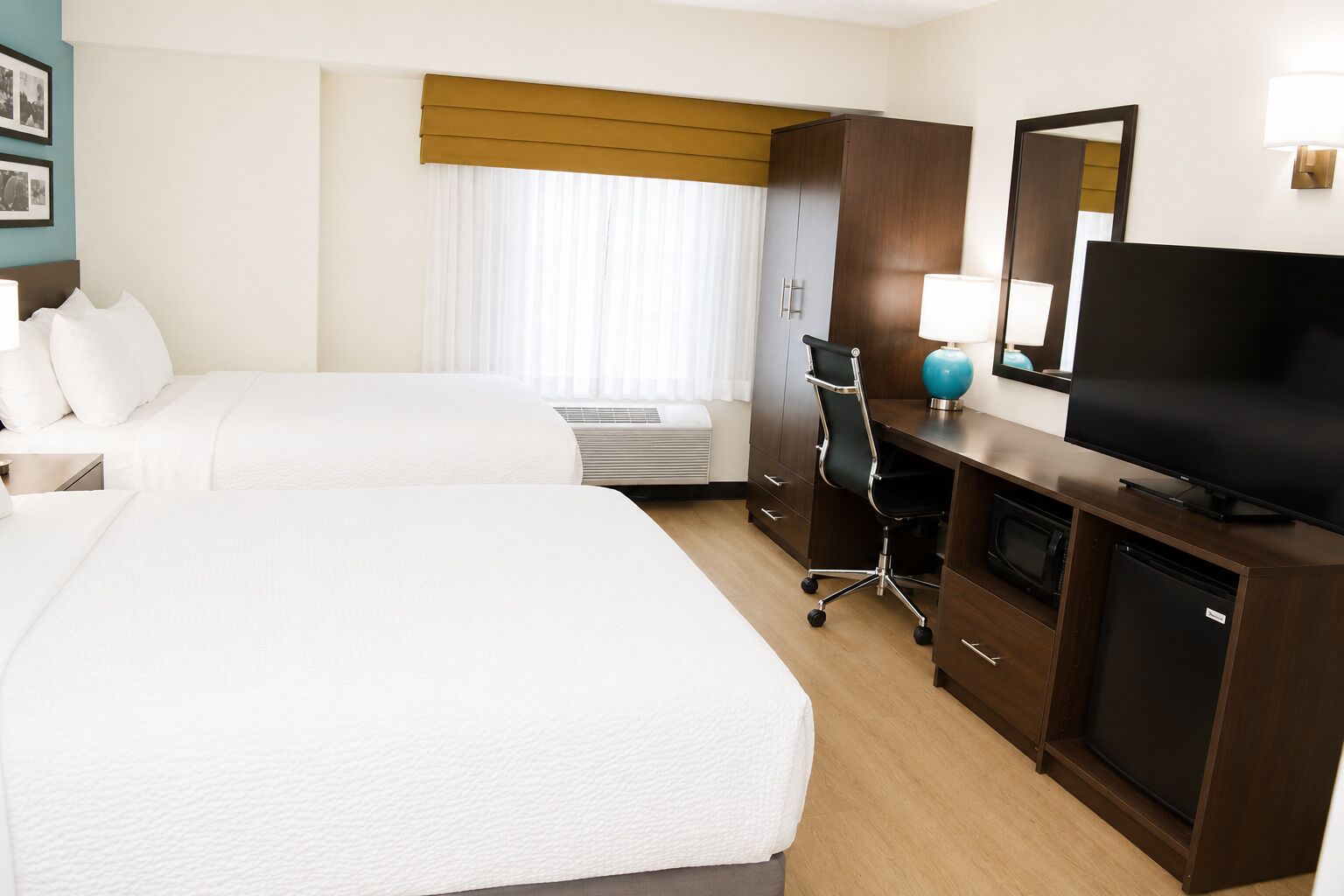 A hotel room with two beds, a desk with a chair, a television, and a minibar.