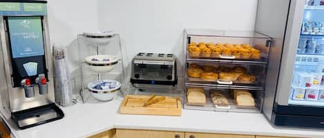 A kitchenette with a waffle maker, toaster, bread, and a refrigerator stocked with beverages.
