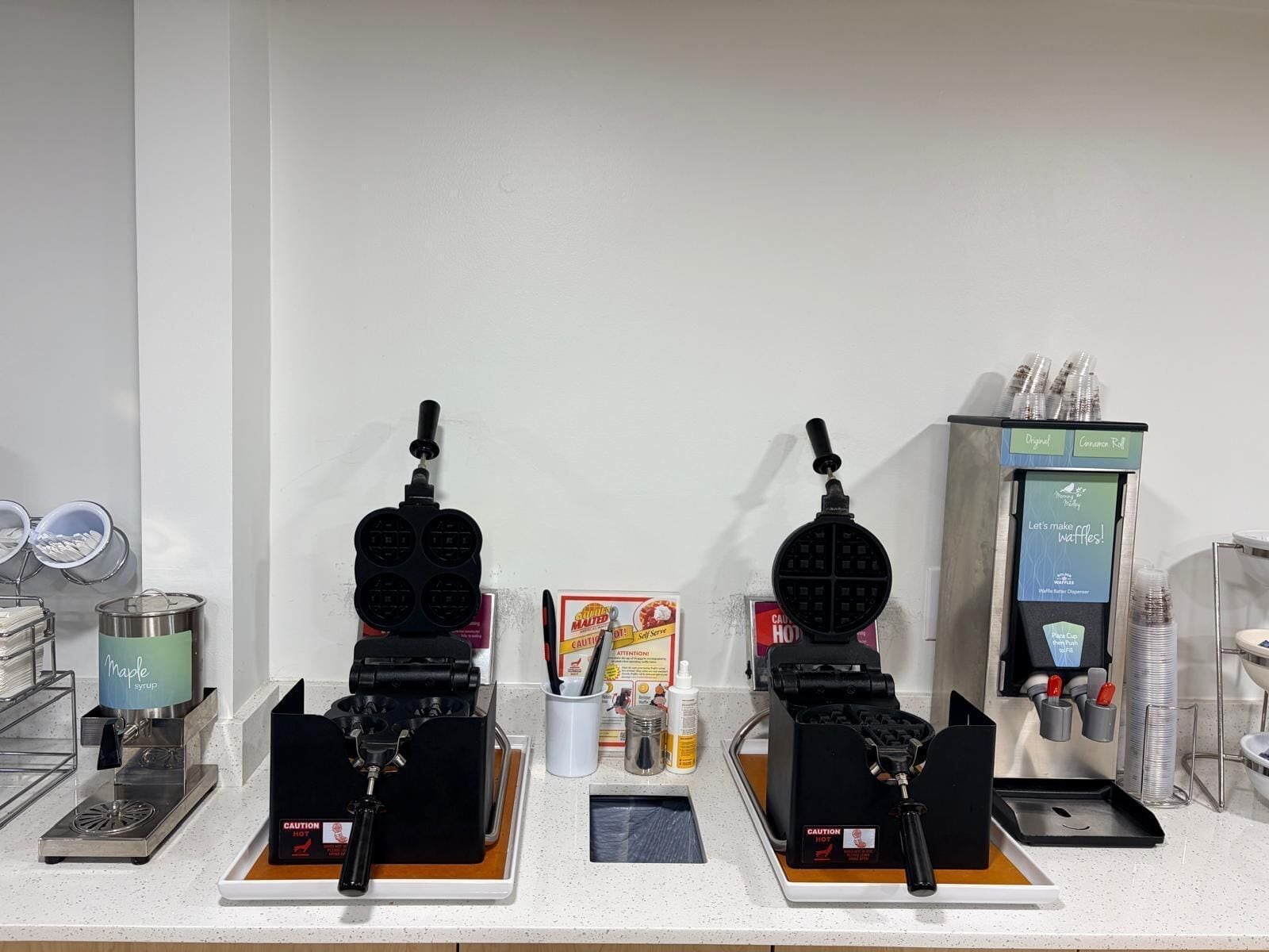 Un buffet proposant des gaufres, avec plusieurs gaufriers, un distributeur de sirop d’érable et une machine à café.