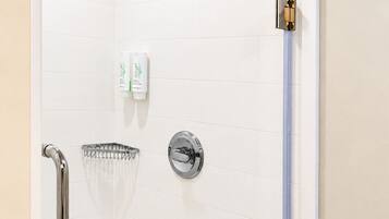Ducha con cabezal de ducha manual, toallero con una toalla blanca y puerta de vidrio para la ducha.