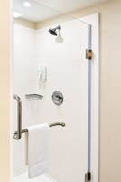 Ducha con cabezal de ducha manual, toallero con una toalla blanca y puerta de vidrio para la ducha.
