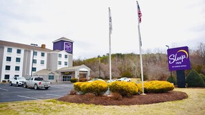A Sleep Inn by Choice Hotels with a parking lot, a building with a sign, and two flagpoles with flags. - Sleep Inn Staunton (Staunton)