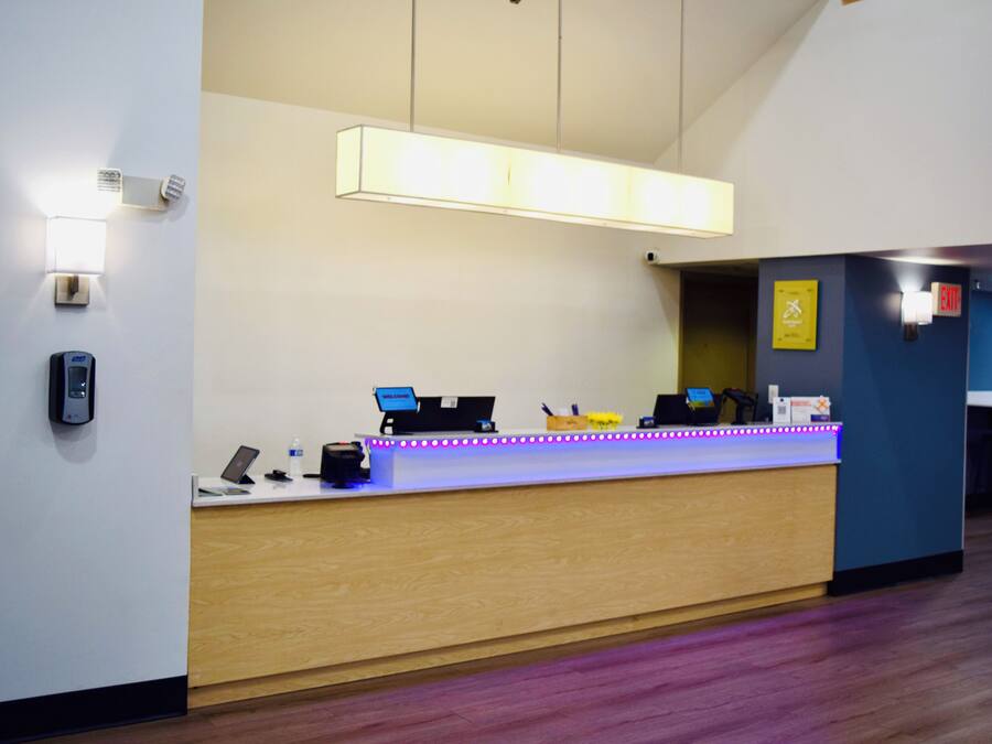 A reception desk with a computer, a phone, and a small counter. There is a wall-mounted light above the desk and a yellow sign on the wall.