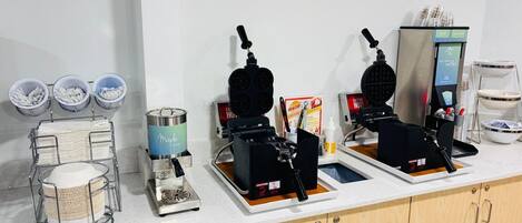 Et tekøkken med kaffemaskine, vaffeljern og en dispenser til ahornsirup.