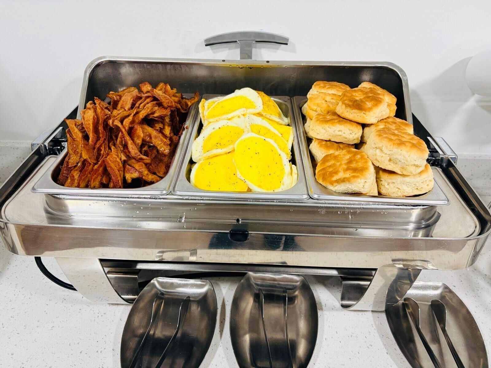 A buffet with bacon, eggs, and biscuits.