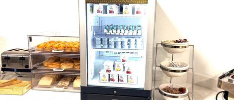 Una estación de desayuno con refrigerador, tostadora y recipientes con comida.