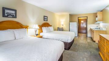 Een hotelkamer met twee bedden, een bureau, een koelkast en een badkamer in de achtergrond.