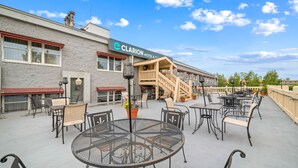 An outdoor patio area with round metal tables and chairs, a staircase leading to a second floor, and a sign for the Clarion Hotel & Suites.