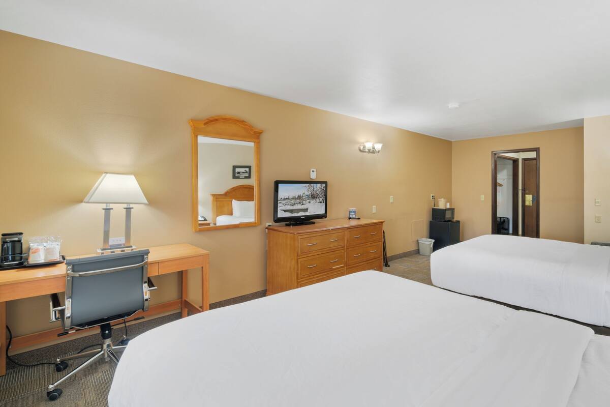 A hotel room with two beds, a desk with a computer, a television, a dresser, and a mirror.