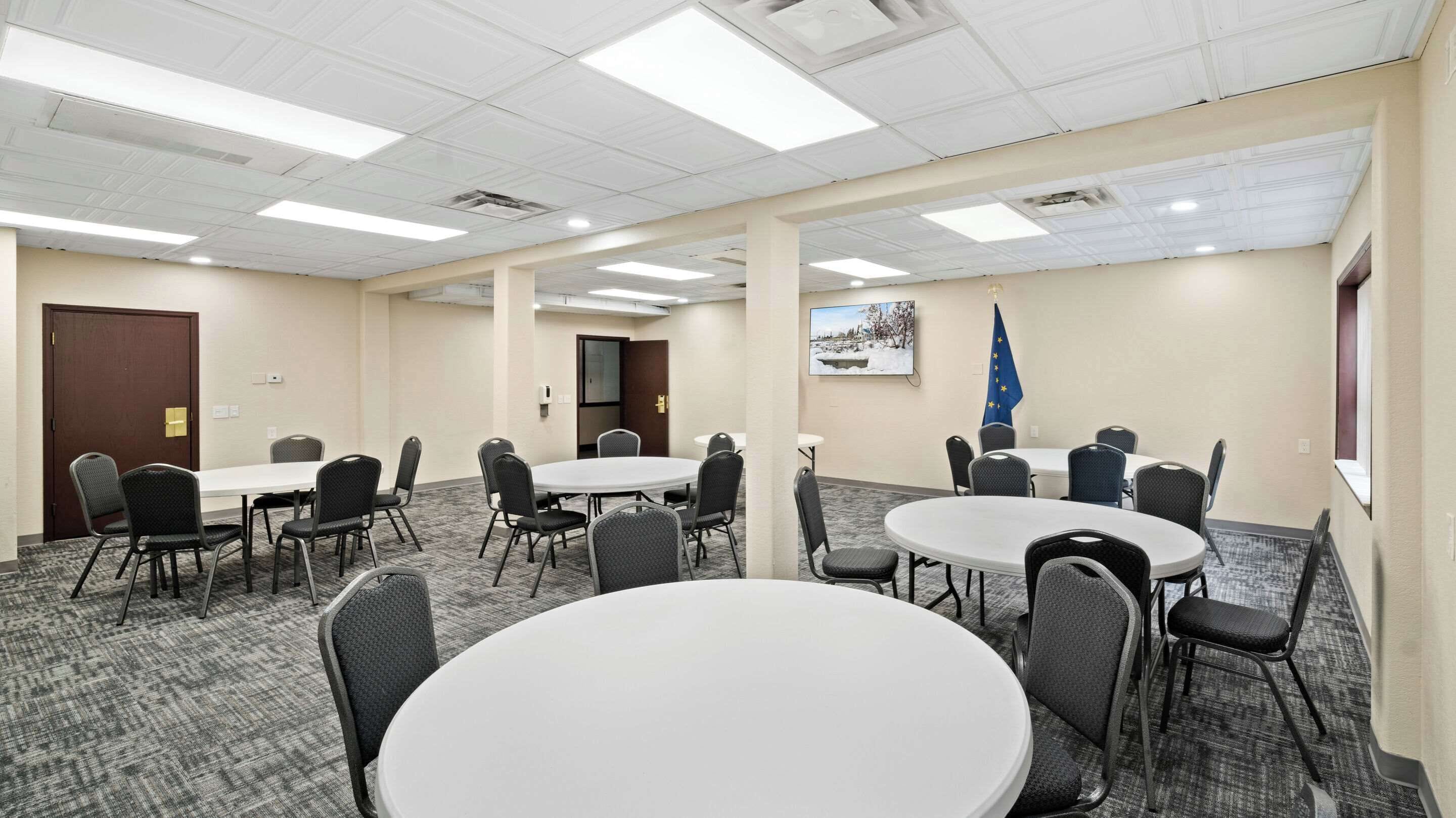 Un salón de conferencias con varias mesas y sillas, una puerta y una bandera en la pared.