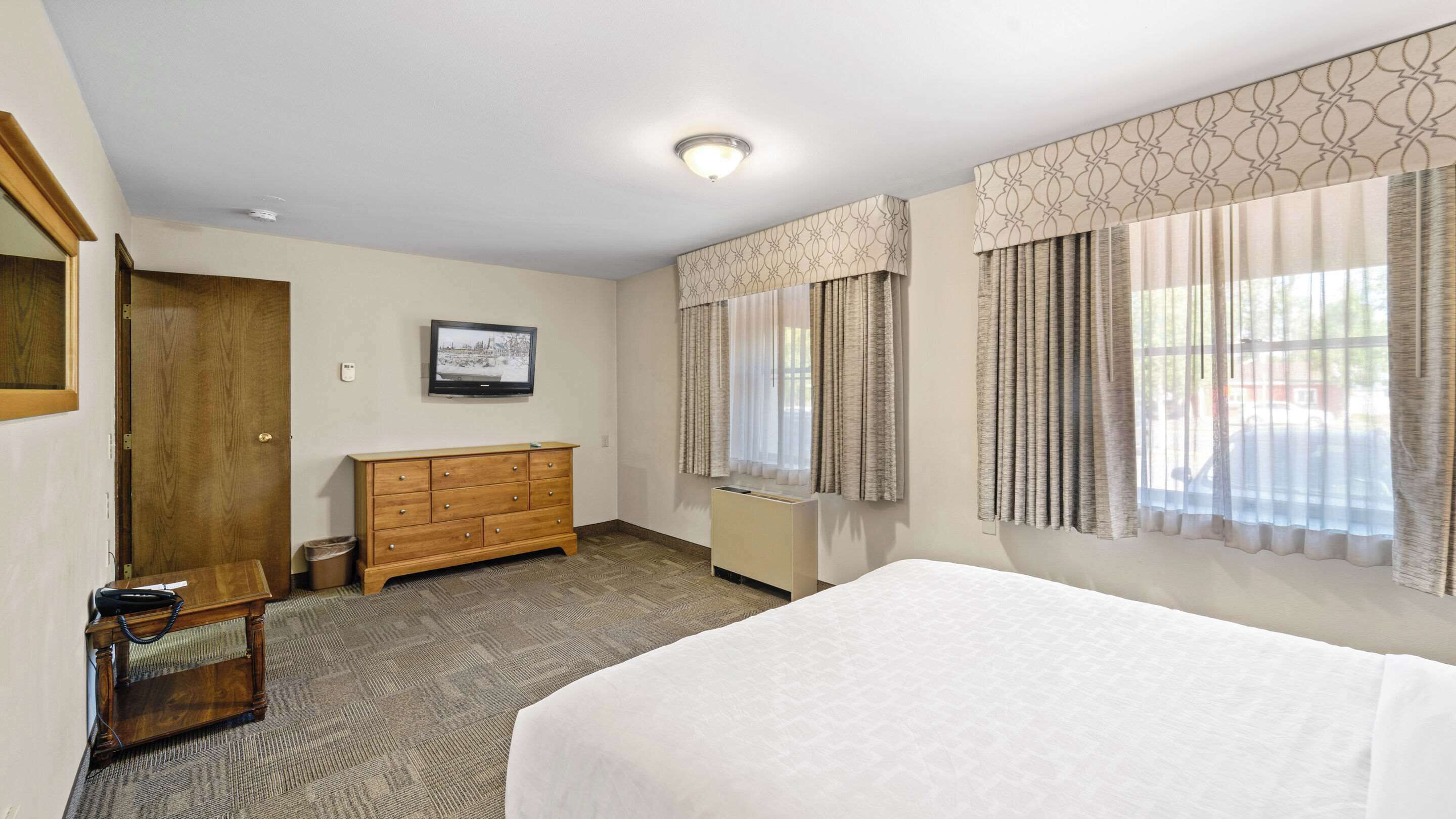 Une chambre d’hôtel avec un lit, une commode en bois, un téléviseur et une fenêtre avec des rideaux.