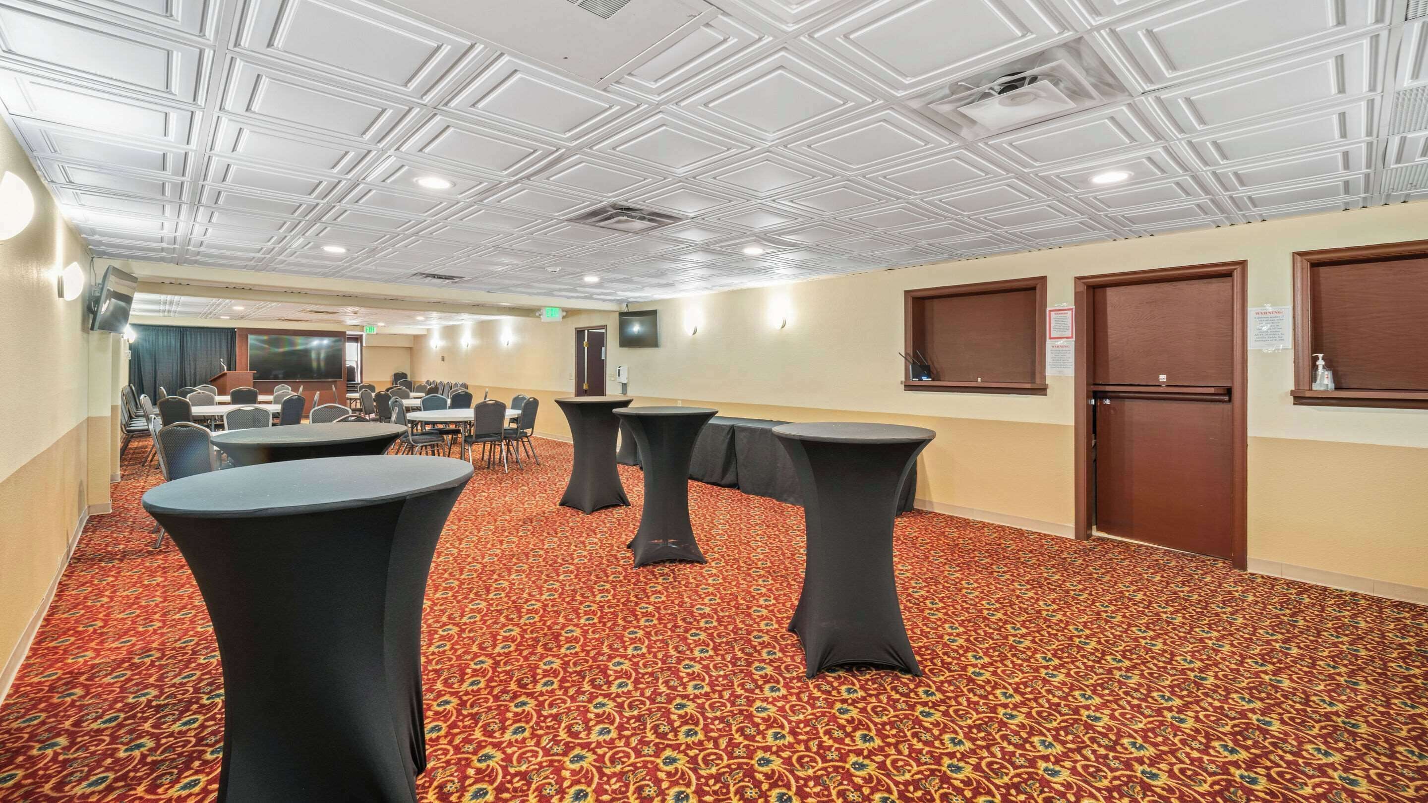 A conference room with tables and chairs, a patterned carpet, and a white ceiling with recessed lighting.