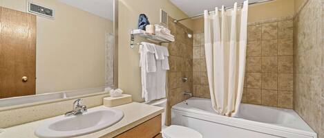 A bathroom with a sink, toilet, and bathtub. There is a towel rack with towels and a bag.
