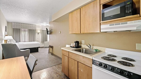A compact hotel room with a kitchenette, including a microwave, stove, and sink.