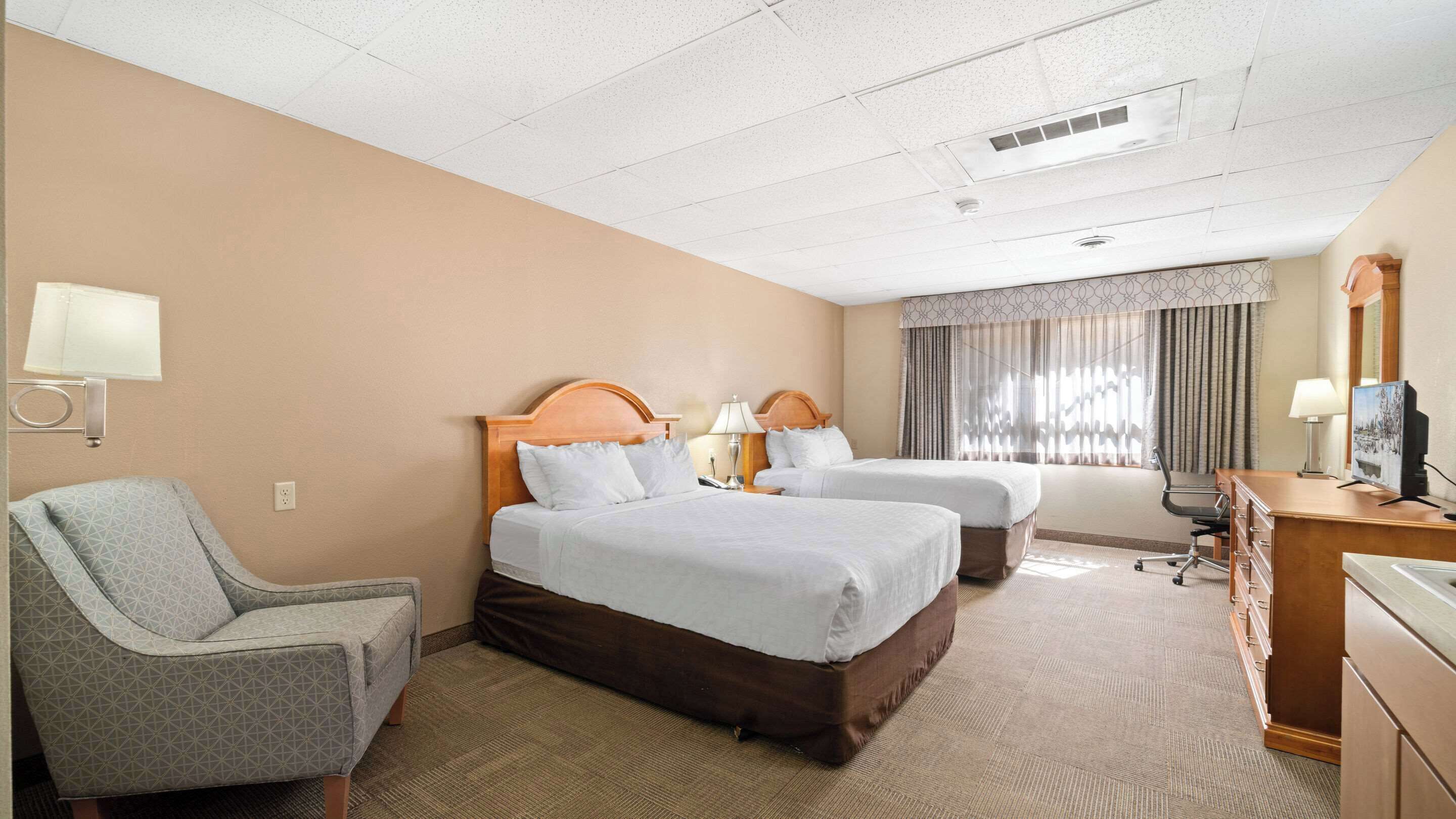 A hotel room with two beds, a desk, a chair, and a television.