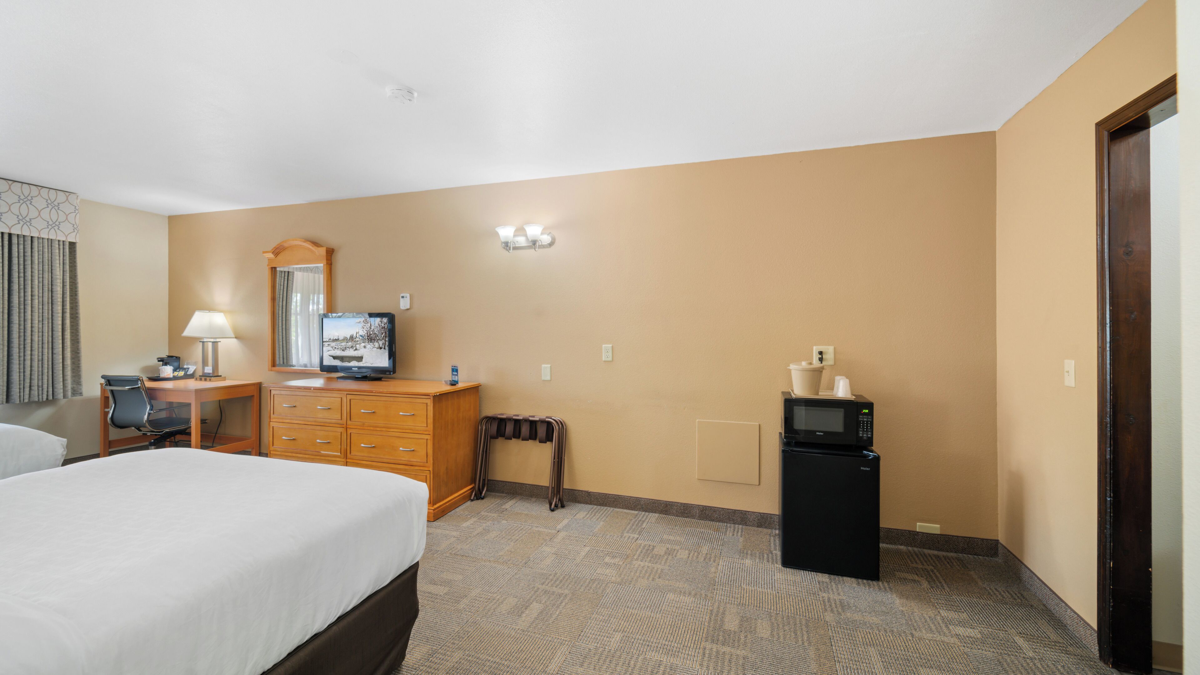A hotel room with a bed, a desk with a lamp, a television, a microwave, and a refrigerator.