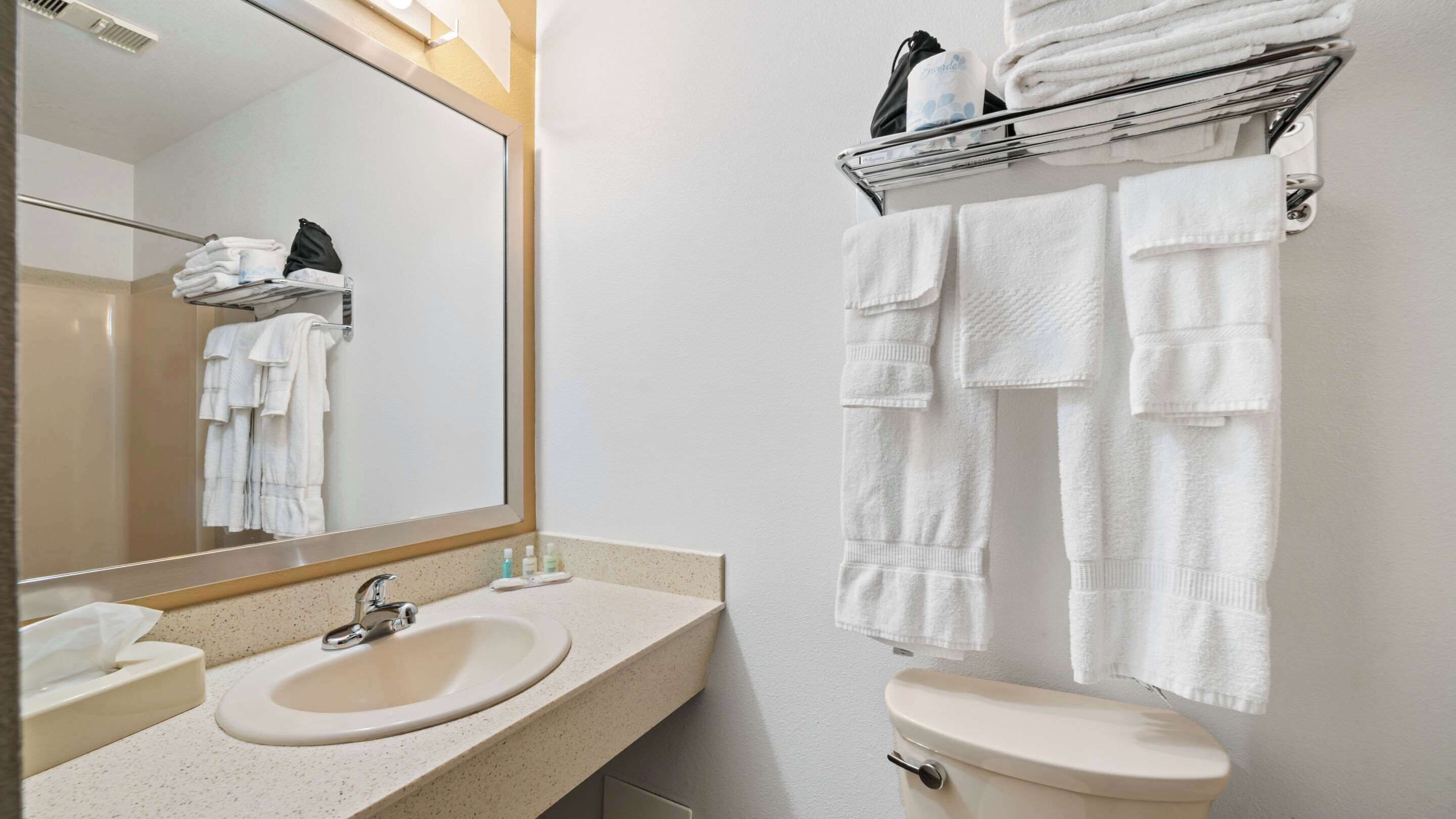 A bathroom with a sink, toilet, and a mirror. There are towels hanging on a rack and a shelf with toiletries.
