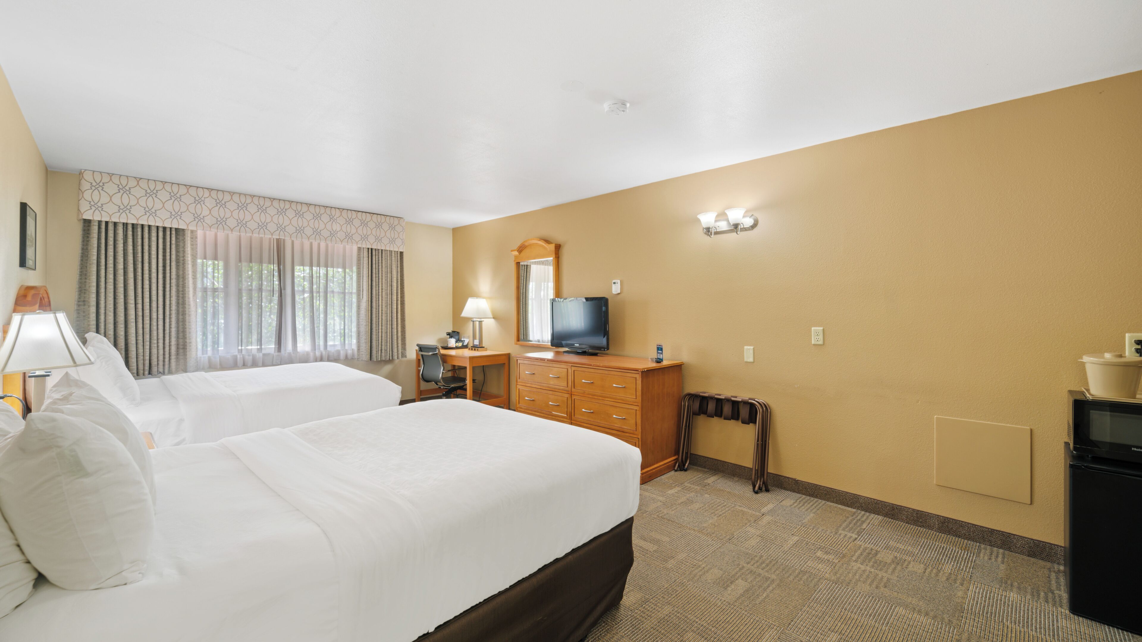 A hotel room with two beds, a desk with a computer, a television, and a dresser.