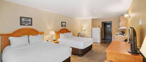 A hotel room with two beds, a desk, a refrigerator, and a television.