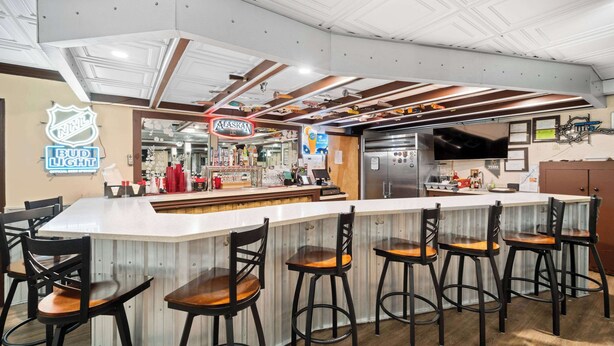A bar area with a counter, stools, and a refrigerator.