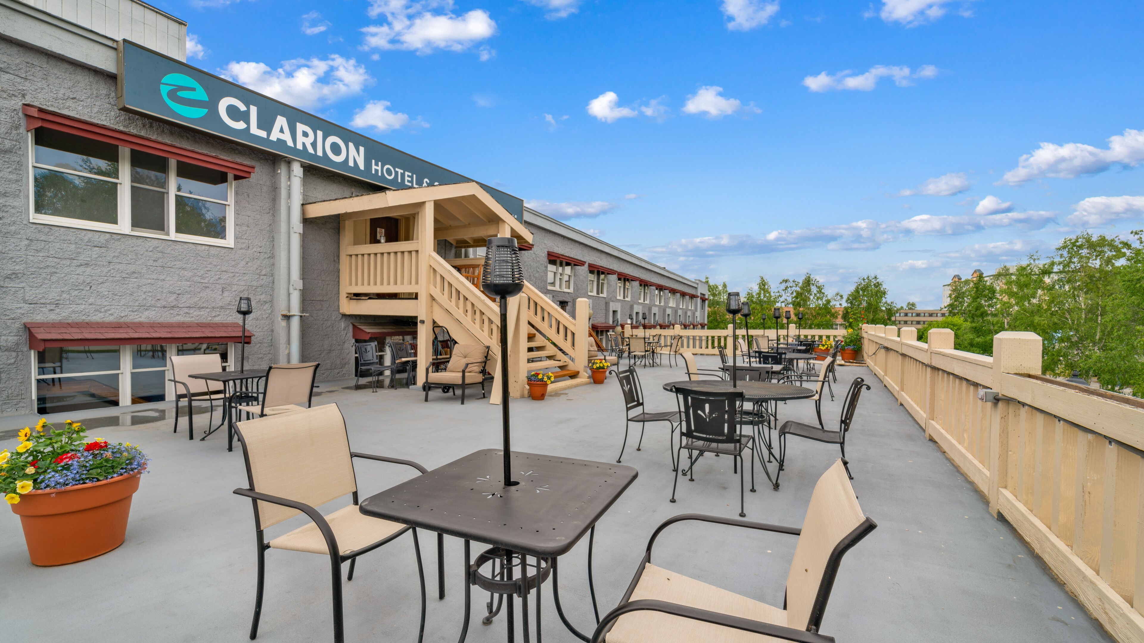 An outdoor patio area with tables and chairs, a staircase leading to an upper level, and a sign for Clarion Hotel.