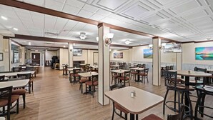 A spacious restaurant with multiple tables and chairs, a wooden floor, and a high ceiling with decorative molding.