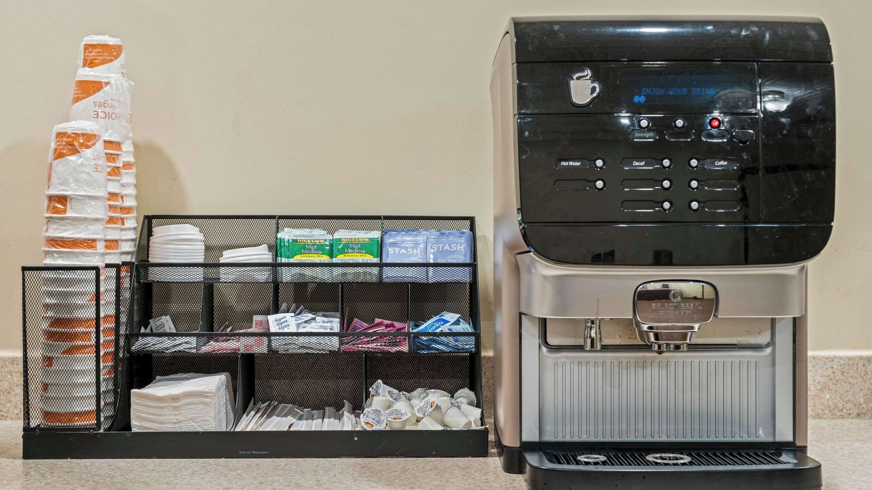 A coffee machine and a dispenser with various coffee pods and paper cups.