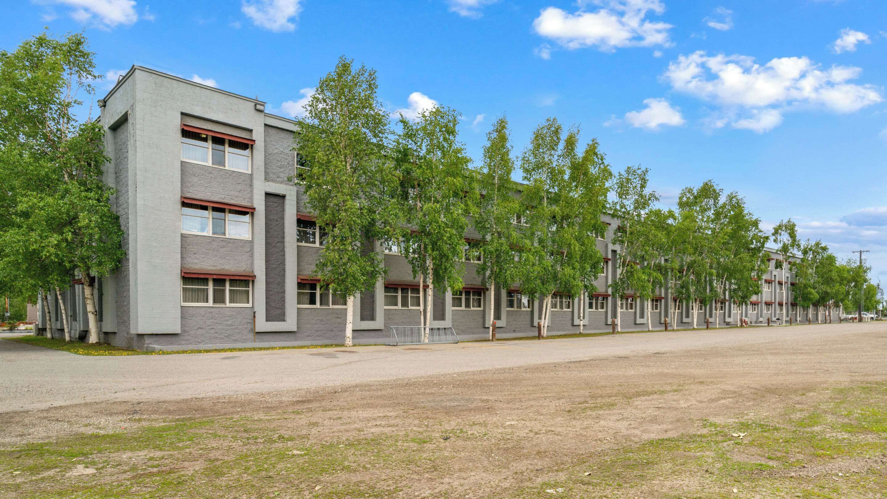 A multi-story building with a flat roof, large windows, and a paved ground area.