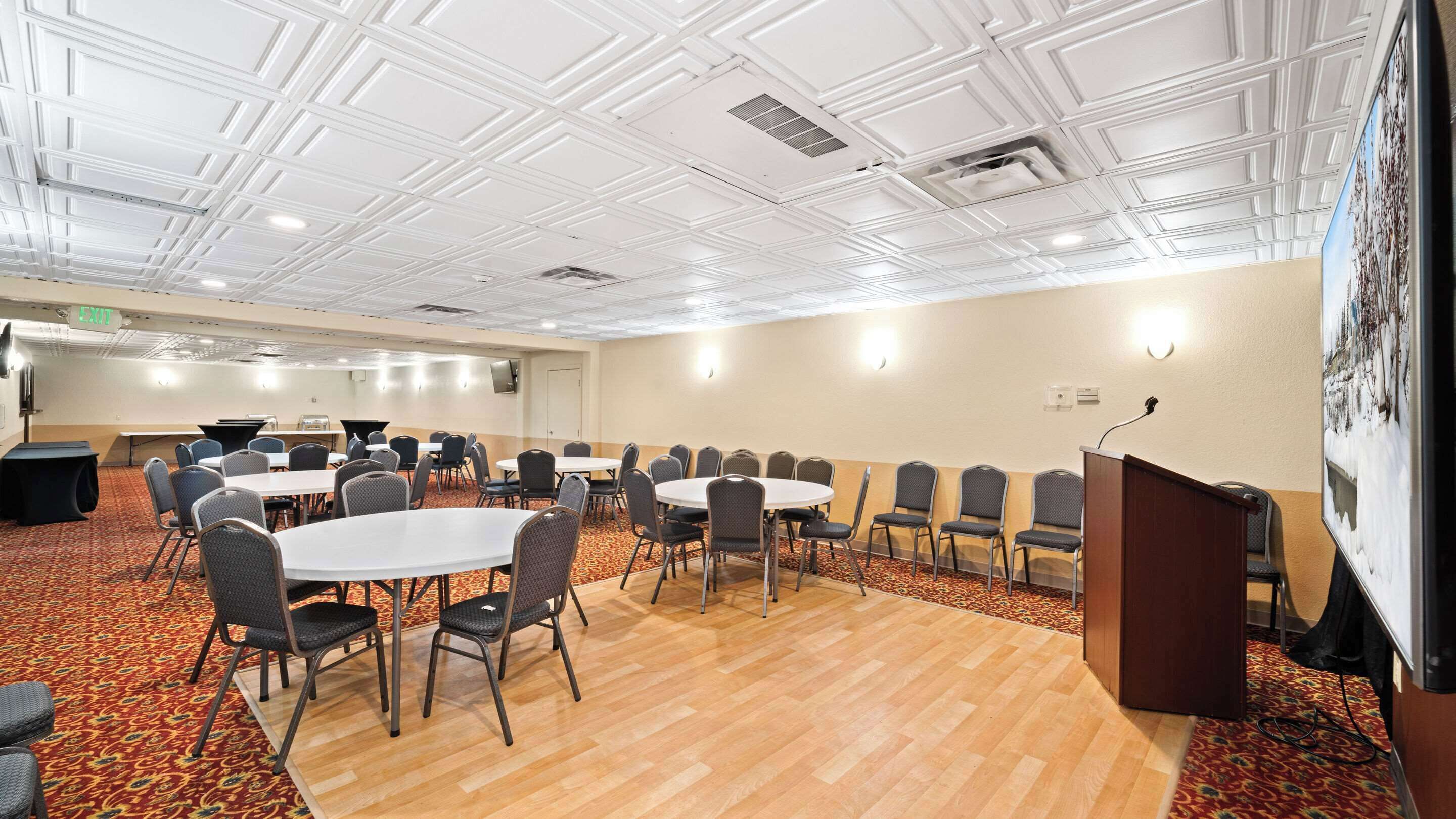 A conference room with round tables and chairs, a podium, and a carpeted floor.