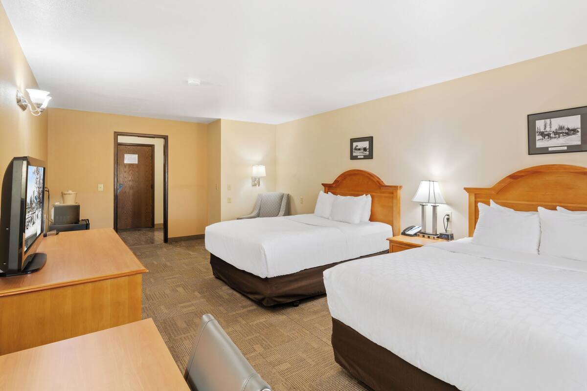 A hotel room with two beds, a desk, a TV, and a door leading to another room.