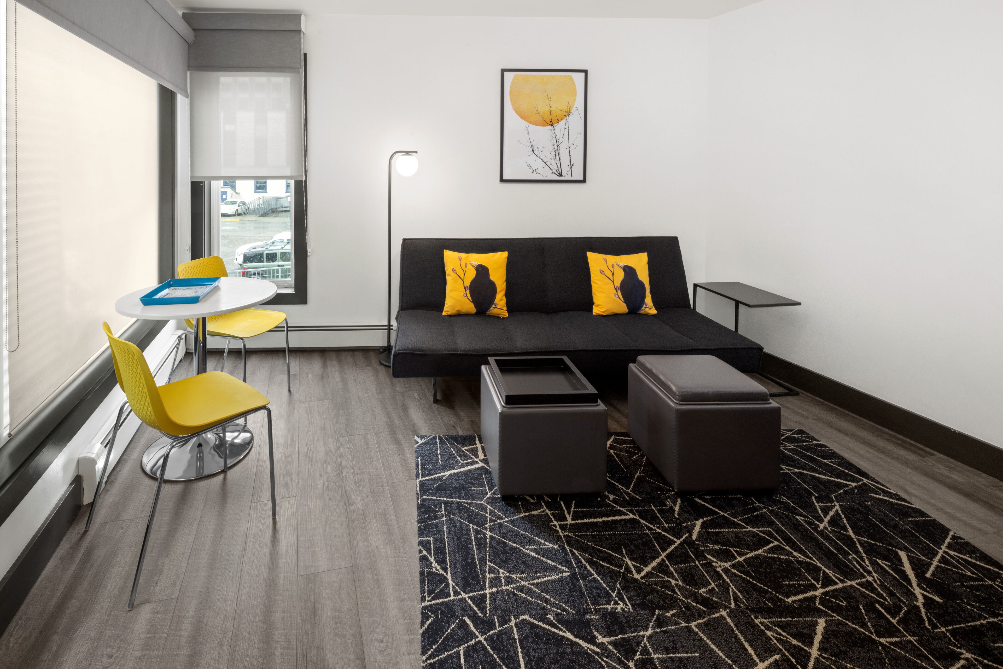 A modern room with a sofa, two yellow chairs, a small table, and a patterned rug.