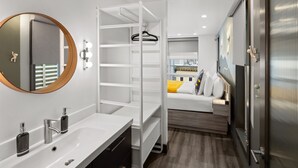 A modern bathroom with a white vanity, a round mirror, and a built-in shelving unit. - The Silverbow Inn (Juneau)