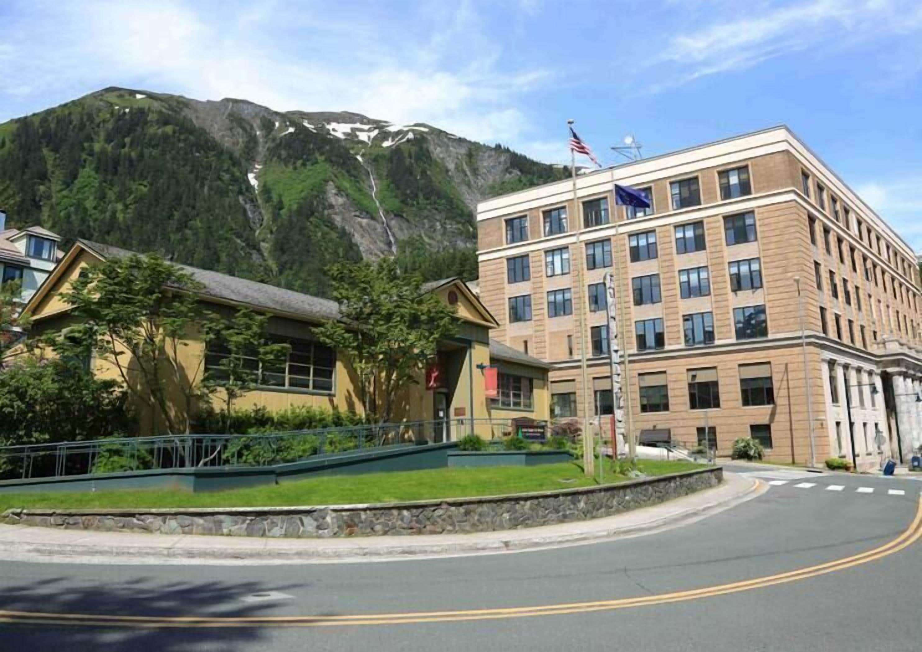 A hotel with a mountain backdrop, featuring a modern building with multiple windows and a flagpole with flags.