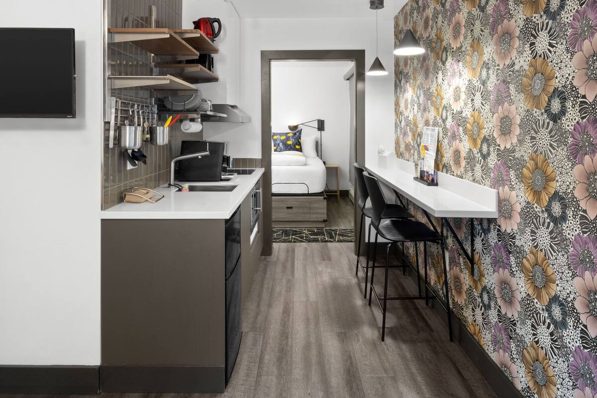 A compact kitchen with modern appliances, a dining area with a small table and chairs, and a bedroom visible through an open door.