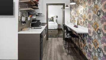 Cocina compacta con electrodomésticos modernos, comedor con una mesa pequeña y sillas, y un dormitorio visible a través de una puerta abierta.