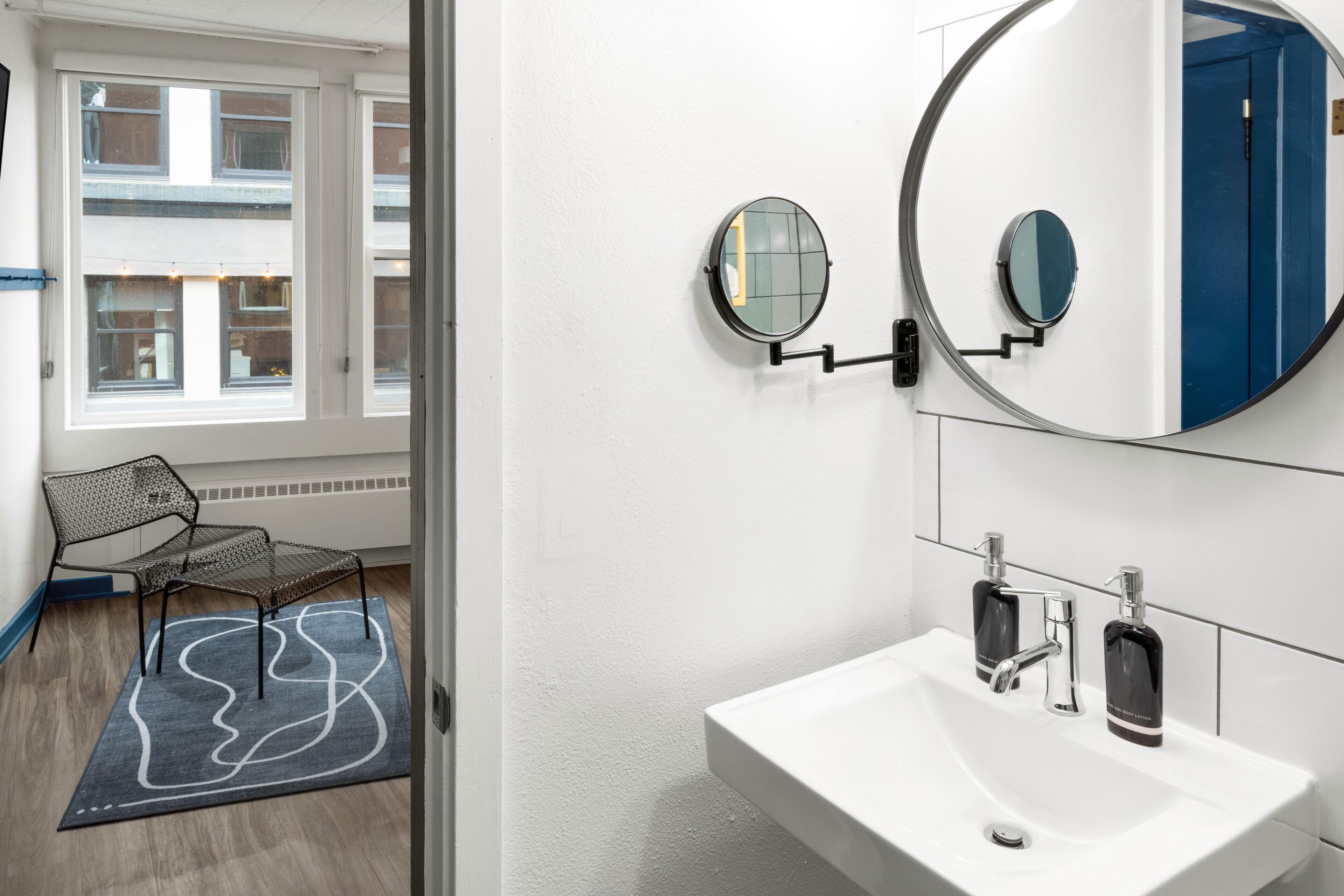 A bathroom with a white sink, two round mirrors, and a blue door.