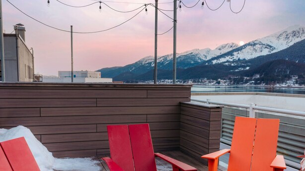 A deck with red chairs, a fire pit, and a view of mountains and a lake. - The Silverbow Inn (Juneau)