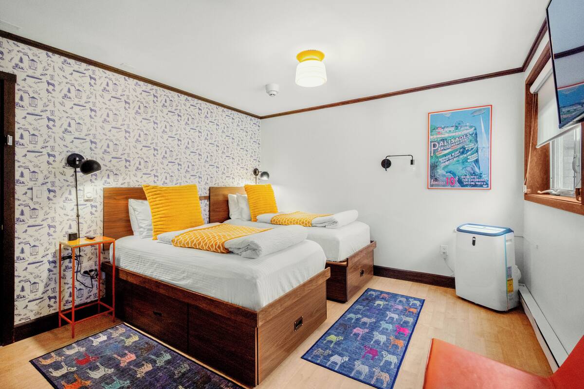 A bedroom with a wooden bed, two bedside tables, a nightstand, a white radiator, a poster on the wall, and a patterned rug.