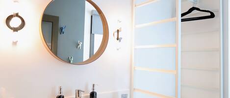 A bathroom with a round mirror, two sinks, and a white vanity.