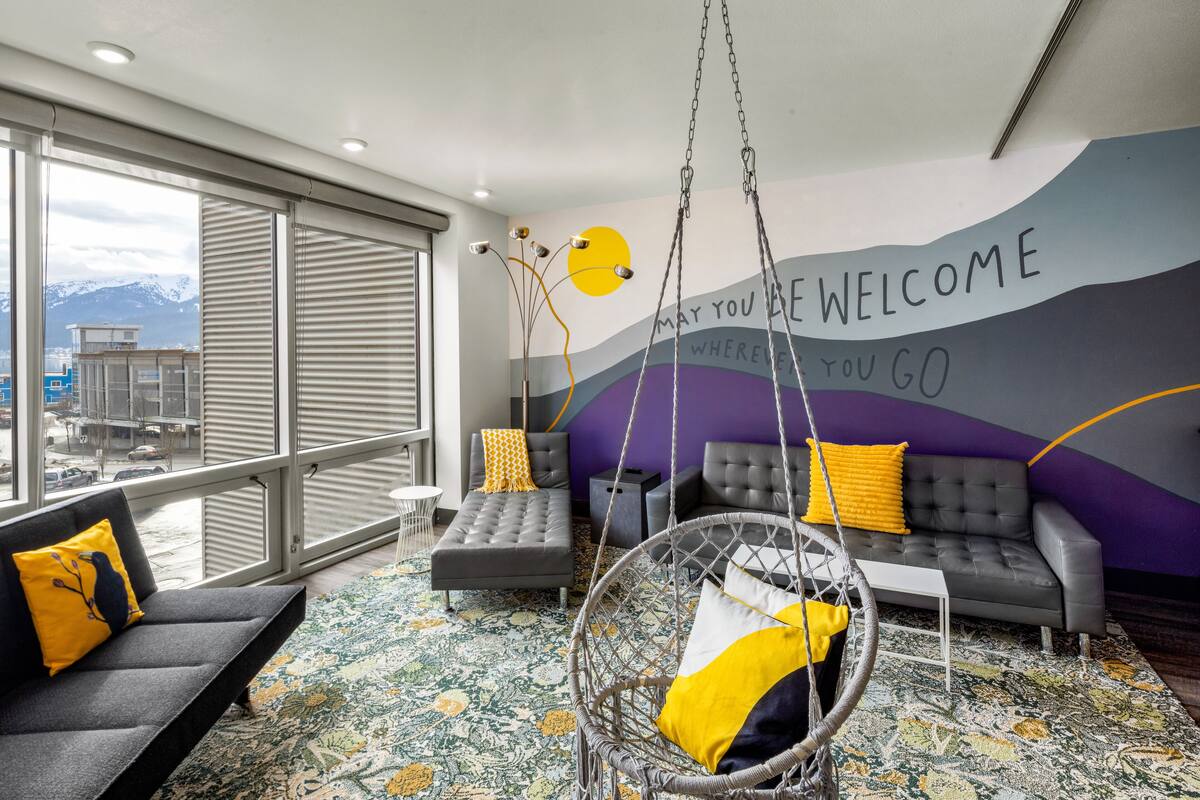 A modern hotel room with a large window, a sofa, a hanging chair, and a colorful wall mural.