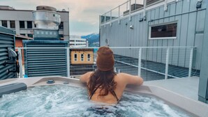 A person relaxing in a hot tub on a rooftop with a cityscape view. - The Silverbow Inn (Juneau)