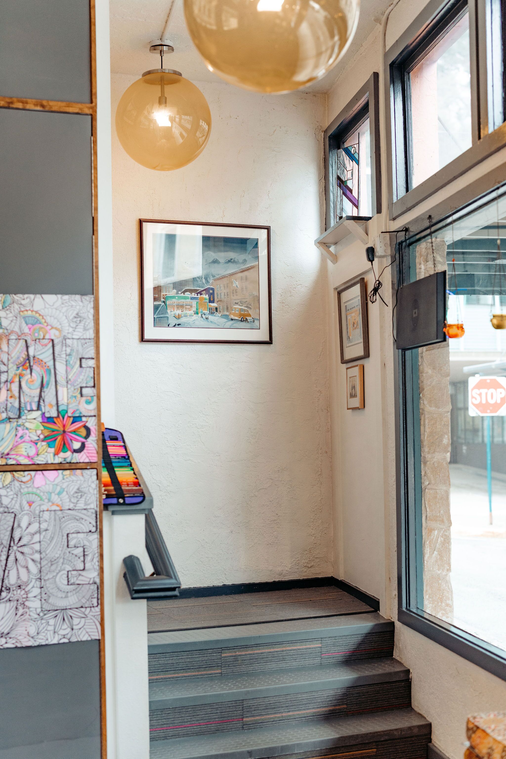 A staircase leading to a room with a view of the street, a framed picture on the wall, and a hanging light fixture.