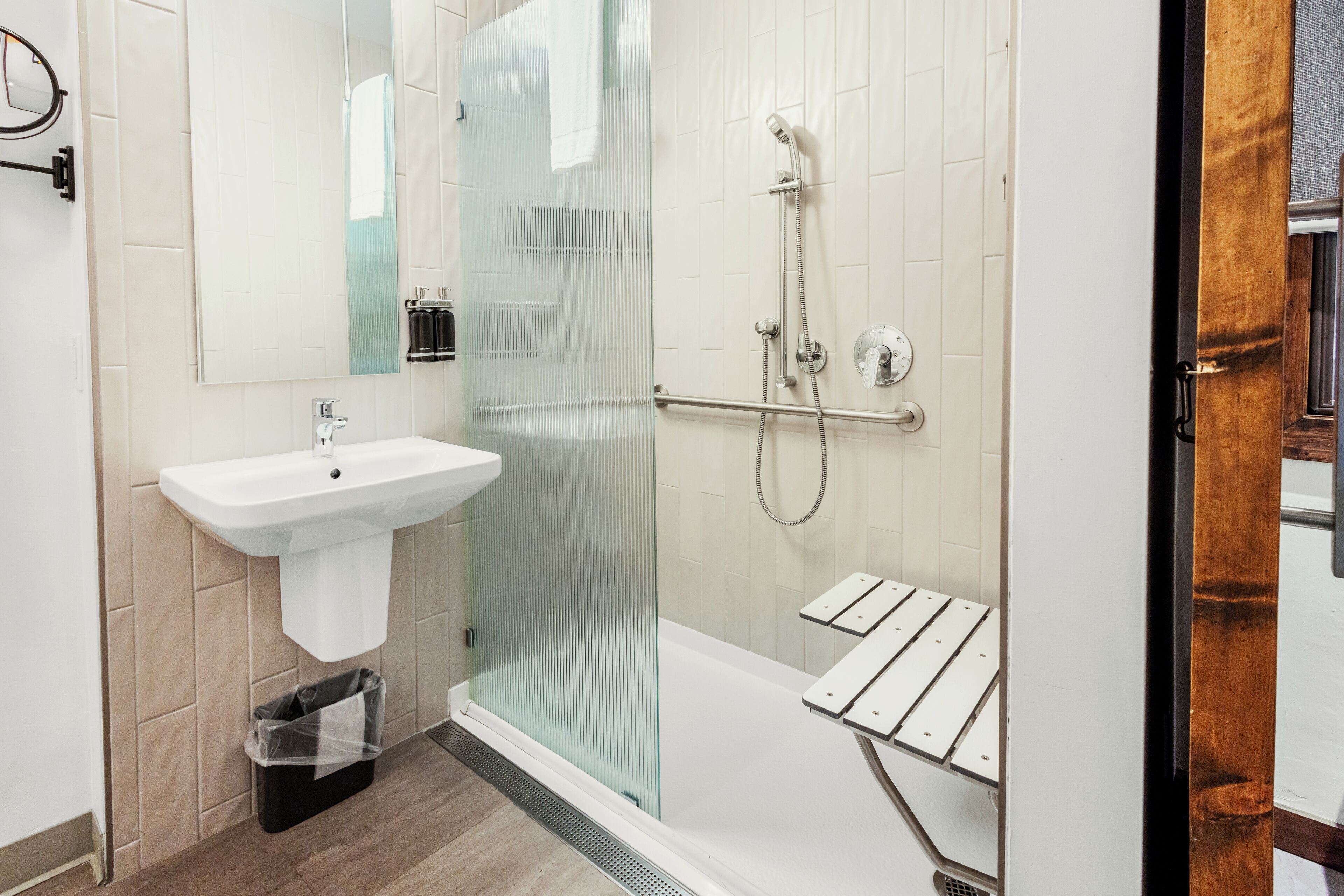 Un baño moderno con cabina de ducha de vidrio, un lavamanos blanco y piso de madera.